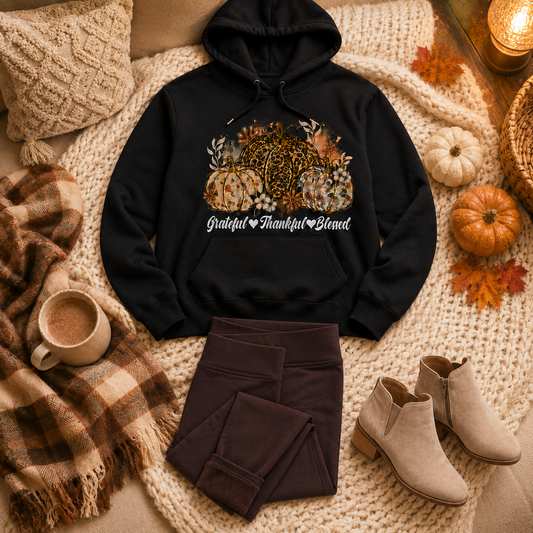 Black Grateful Thankful Blessed pumpkin graphic hoodie styled with folded brown fleece-lined leggings and taupe ankle booties in a cozy fall home flat lay.