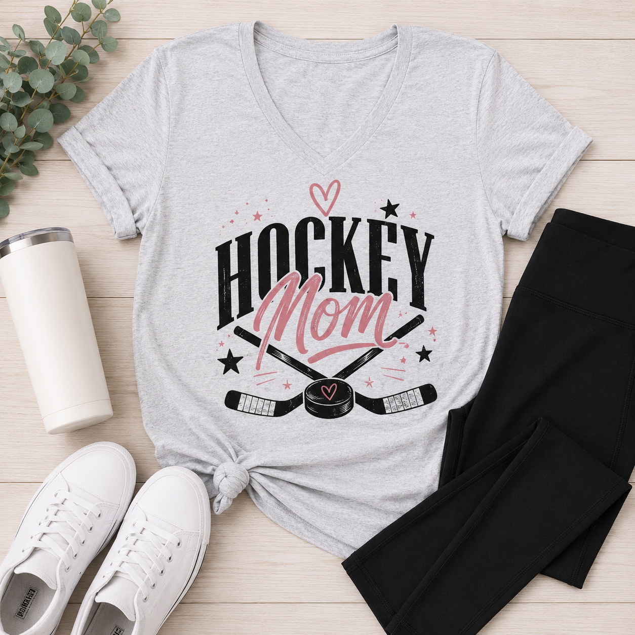 Heather gray v-neck Hockey Mom graphic tee featuring a black and pink hockey design styled with black leggings and white sneakers.