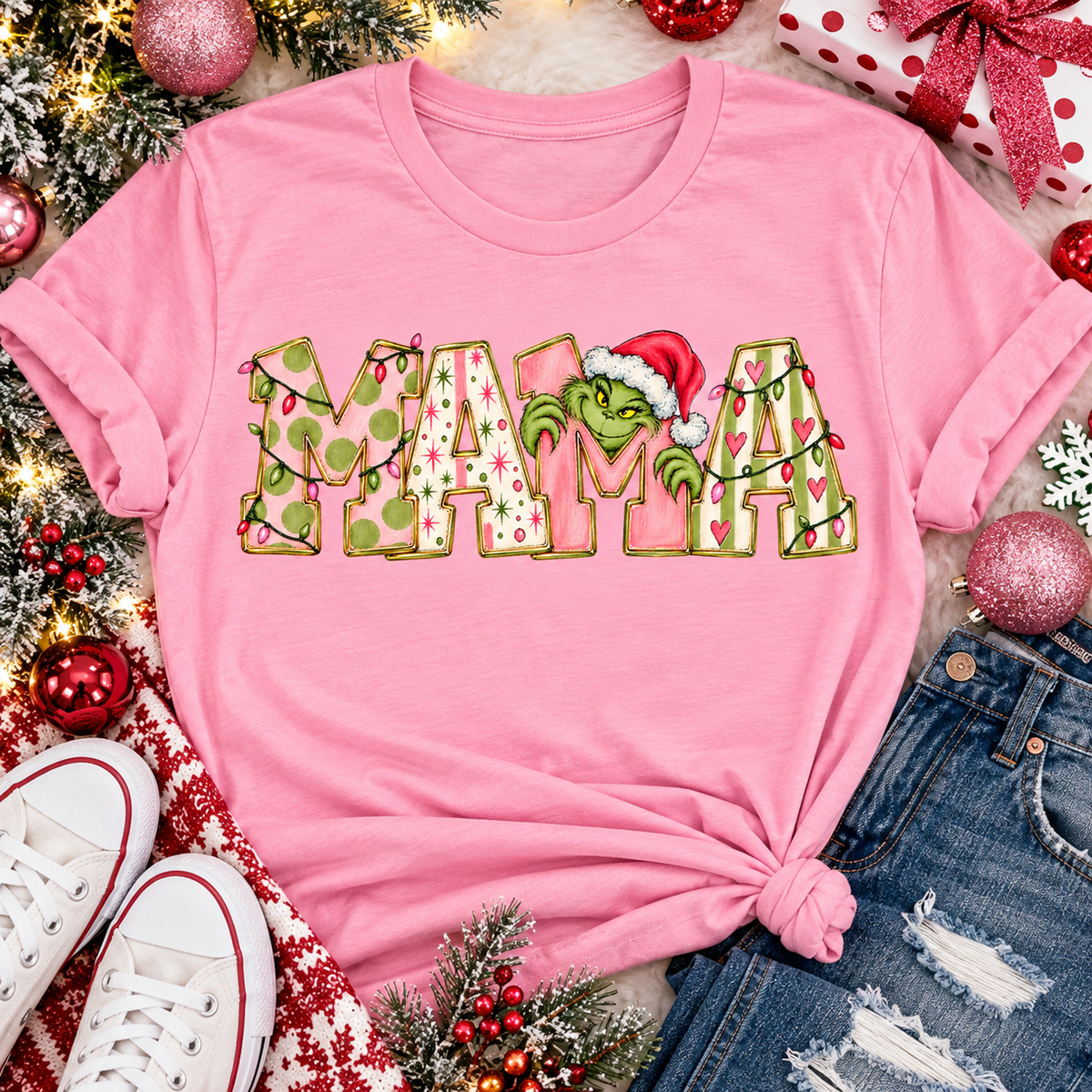 Christmas MAMA graphic shirt featuring pink and green patterned lettering, colorful holiday lights, and a Grinch-inspired character wearing a Santa hat.